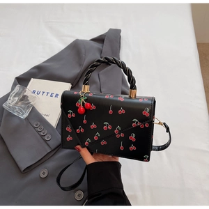 Détail du sac cerise avec poignée tressée, quincaillerie dorée et pendentif cerise