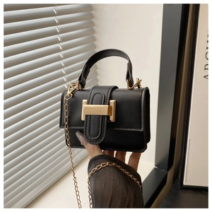 Detail of black matte leather mini bag featuring gold H-shaped buckle and metal chain strap