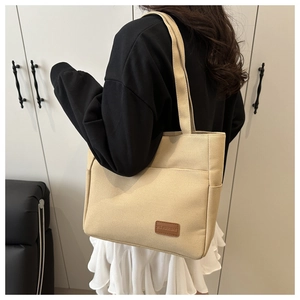 Detail of large beige canvas tote bag with brown leather logo patch and shoulder strap