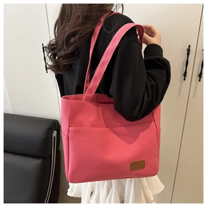 Detail of pink canvas tote bag with front pocket and leather logo patch on model's shoulder