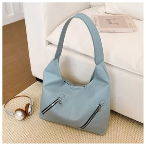Detail of dusty blue leather tote bag with silver zippers on a minimalist woven rug