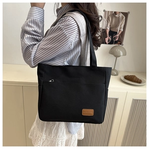 Close-up of black canvas tote bag with front pocket and leather brand tag in a home setting