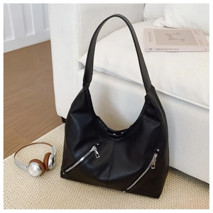 Detail shot of black pebbled leather tote bag with silver zippers on a white sofa