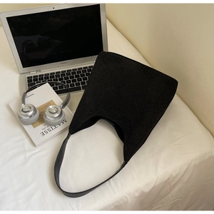 Macro shot of black suede hobo bag featuring studded rivets and wide strap on white bedding