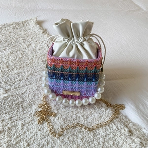 Detail of colorful woven bucket bag with pearl handle and golden chain strap