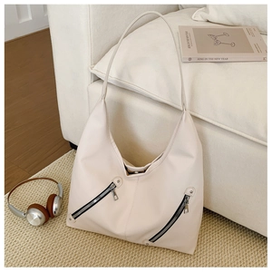 Close-up of off-white lychee pattern tote bag with decorative zippers on a sofa