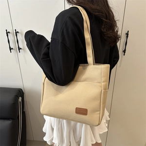 Minimalist canvas tote bag with brown leather patch and side pockets for women