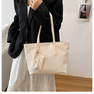 Detail of cream tote bag with embossed pattern and matching square charm hanging on the strap