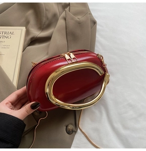 Detail of red mini clutch with large gold C-shaped metal handle and chain strap