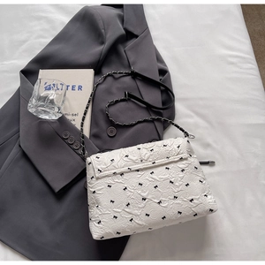 Detail of white textured shoulder bag with black bow embroidery and leather chain strap