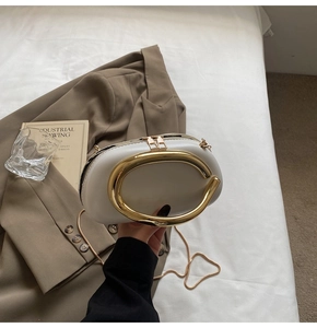 Detail of a creamy oval evening bag with large gold C-handle and delicate chain strap