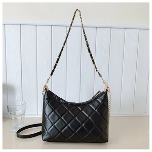 Close-up of black quilted shoulder bag with gold chain strap on a white wooden background