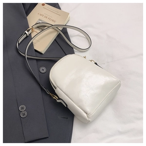 Detail view of white PU leather crossbody bag with gold zipper and textured surface
