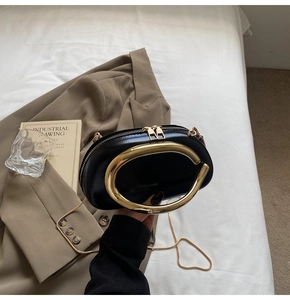 Detail of black semi-circular evening bag with oversized gold ring handle and metal chain