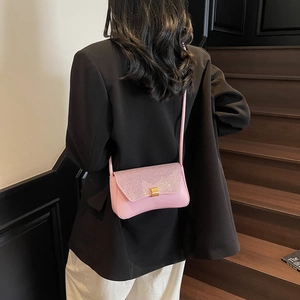 Sac baguette rose en cuir avec paillettes et boucle dorée porté par un mannequin