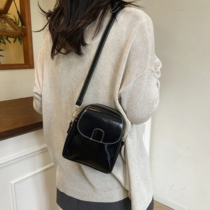 Glossy black mini crossbody bag with white stitching and gold hardware on model