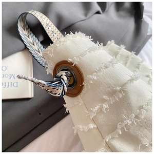 Detail of white textured tote with brown leather eyelet and striped silk scarf ribbon