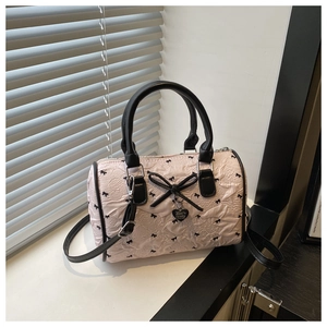 Détail du sac Boston rose clair avec imprimés nœuds noirs et breloque cœur en métal