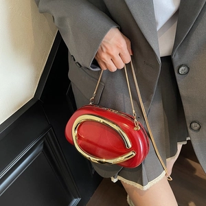 Red oval clutch bag with gold round metal handle and chain strap carried by a model