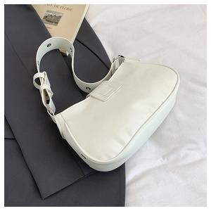Detail view of white PU leather baguette bag with silver grommets on a grey suit background