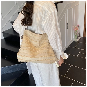 Detail of a large cream fringe tote bag with geometric pattern shoulder strap on a model