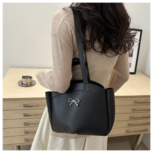 Détail du sac à bandoulière noir en cuir mat avec nœud argenté porté par le mannequin