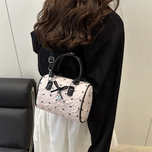 Sac cylindrique rose avec nœuds noirs et pendentif cœur porté à l'épaule du mannequin