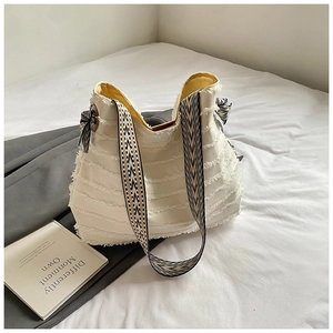 Detail of white canvas tote with fringe tassels and patterned shoulder strap on bedding