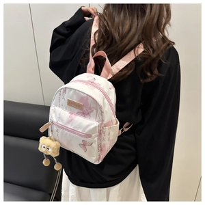 Rear view of a mini backpack with pink butterfly prints and a plush charm on a model