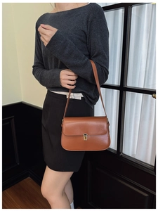 Brown leather baguette bag with a gold buckle worn on shoulder by a model
