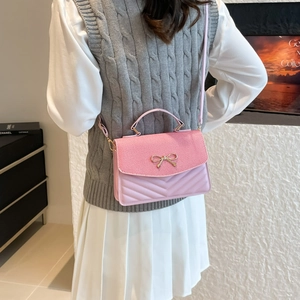 Pink quilted crossbody bag with corduroy flap and gold bow accessory on female model