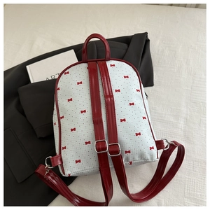 Detail of red ribbon bow print backpack with glossy straps and silver metal buckles