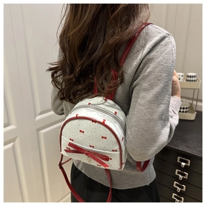 Rear view of a mini white backpack with red bows and thin straps worn by a model