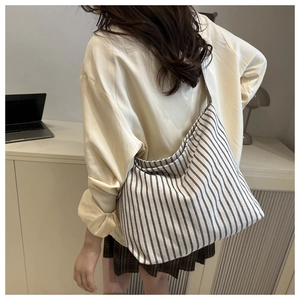 Detail of a large black and white striped canvas tote bag worn by a model in a minimal room