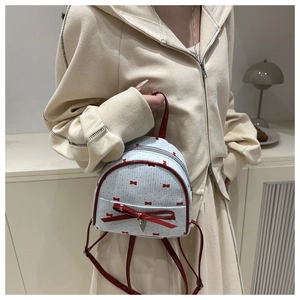 Detail of white backpack with red polka dots and a glossy bow with heart charm