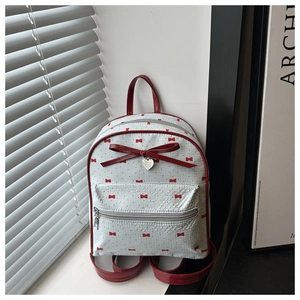 Close-up of white mini backpack with red bow prints and heart metal charm detail