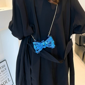 Mini blue metallic acrylic bow bag with gold chain strap shown on model in black coat