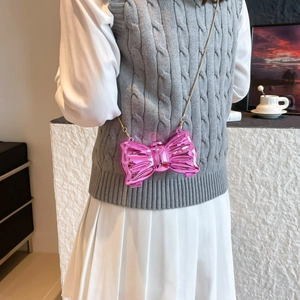 Pink metallic bow-shaped mini crossbody bag with gold chain strap shown on model