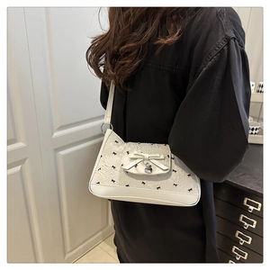 Détail du sac jacquard blanc avec motifs nœuds noirs et pendentif en forme de cœur argenté