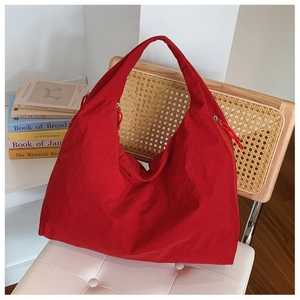 Détail du grand sac cabas en nylon rouge avec texture plissée sur chaise blanche