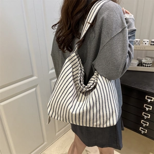 Blue and white striped canvas hobo shoulder bag shown in a casual lifestyle setting
