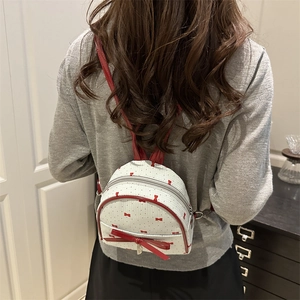 White mini backpack with red bow prints and leather ribbon shown on model's back