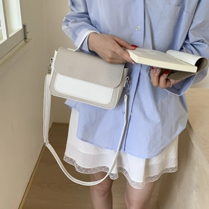 Close-up of woven beige flap and smooth white leather stitching on a small square bag