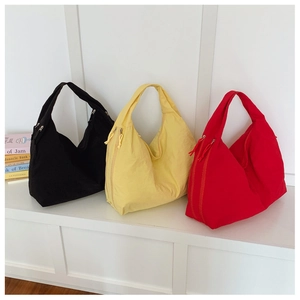 Trois sacs cabas en nylon noir, jaune et rouge exposés sur un banc blanc