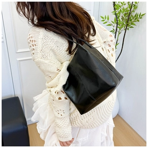 Detail of glossy black bucket tote bag showing its structural design and shoulder drape