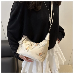 Detailed embroidery of floral and persimmon patterns on a cream silk crossbody bag