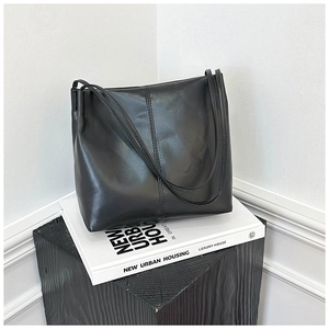 Detail of glossy black leather tote bag with vertical stitching on white backdrop