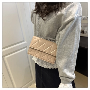 Detail view of beige quilted crossbody bag with silver chain strap worn by a model