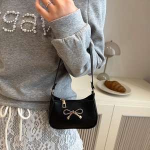 Black litchi grain leather underarm bag with gold bow buckle, shown on a model