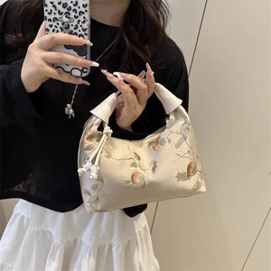 Embroidered beige silk hobo bag with traditional bird and floral patterns held by hand